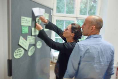 Teilnehmer eines Seminars bringen Notitzen an einem Infoboard an